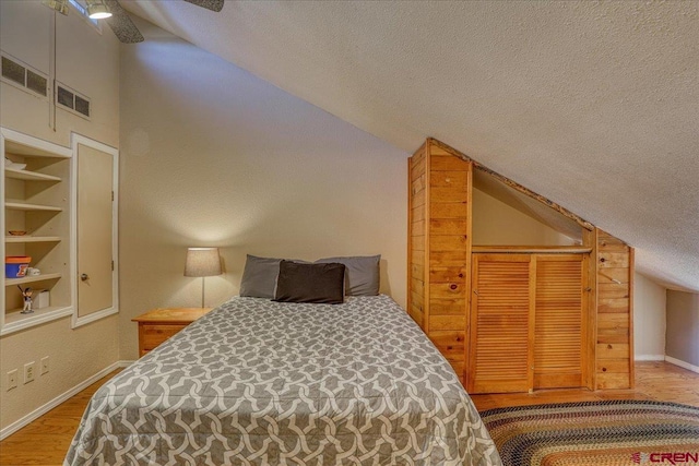 bedroom featuring lofted ceiling, wood-type flooring, and a textured ceiling