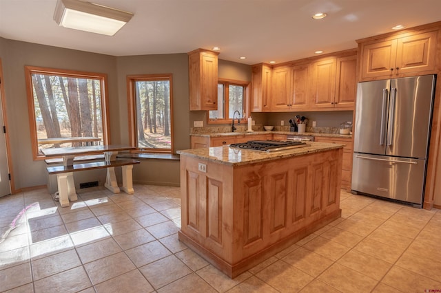 kitchen featuring light brown cabinetry, stainless steel appliances, light stone counters, a kitchen island, and sink