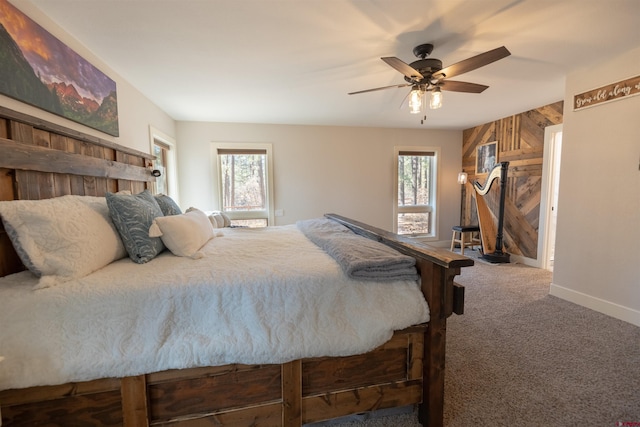 bedroom with ceiling fan, carpet floors, multiple windows, and wooden walls