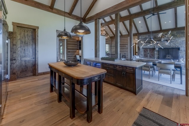 kitchen with light wood-type flooring, pendant lighting, dark brown cabinets, high vaulted ceiling, and beam ceiling