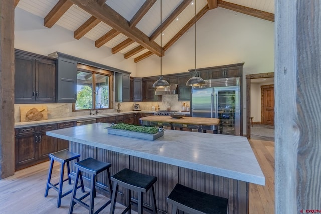 kitchen featuring exhaust hood, stainless steel appliances, decorative light fixtures, a center island, and backsplash