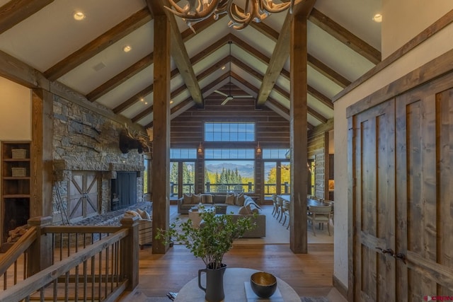 interior space with high vaulted ceiling, wood-type flooring, beamed ceiling, and a stone fireplace