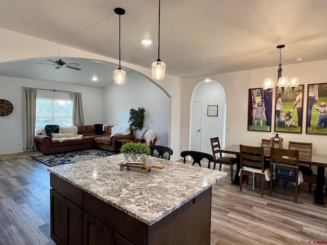 kitchen with light hardwood / wood-style floors, light stone counters, dark brown cabinetry, and pendant lighting