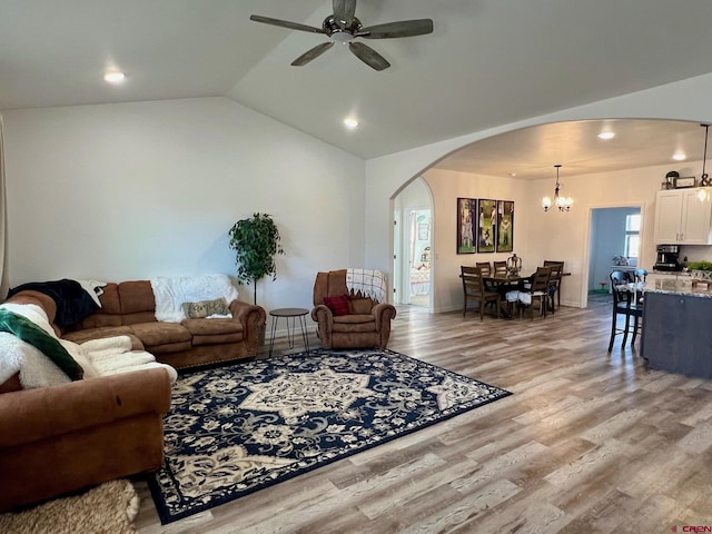 living room with ceiling fan with notable chandelier, light wood-type flooring, and vaulted ceiling