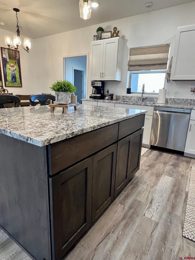 kitchen featuring white cabinetry, light hardwood / wood-style floors, stainless steel dishwasher, light stone counters, and pendant lighting