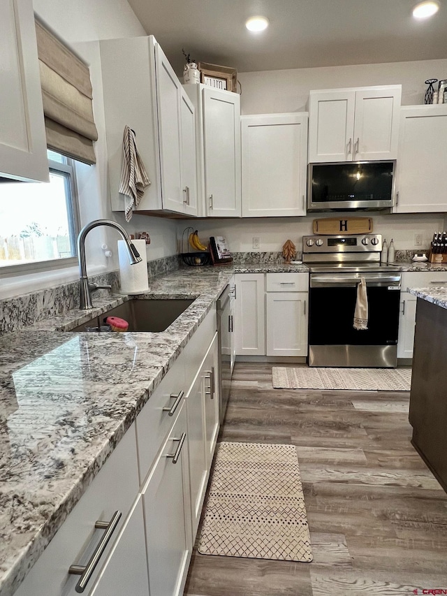 kitchen featuring hardwood / wood-style floors, sink, light stone counters, appliances with stainless steel finishes, and white cabinets