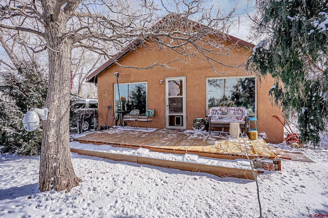 snow covered back of property with a deck and an outdoor living space