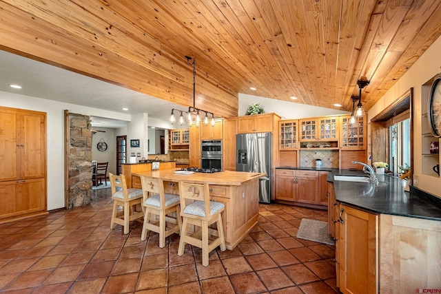 kitchen with decorative light fixtures, a center island with sink, appliances with stainless steel finishes, glass insert cabinets, and wood ceiling