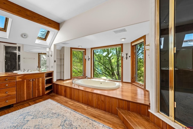 full bath with visible vents, lofted ceiling with skylight, vanity, wood finished floors, and a bath