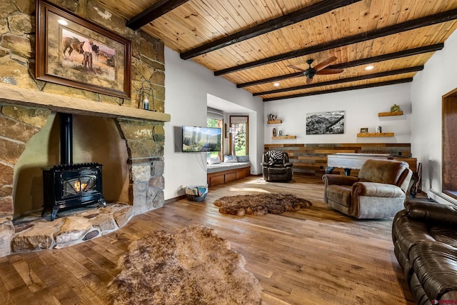 living room with ceiling fan, wood finished floors, wood ceiling, beam ceiling, and a wood stove