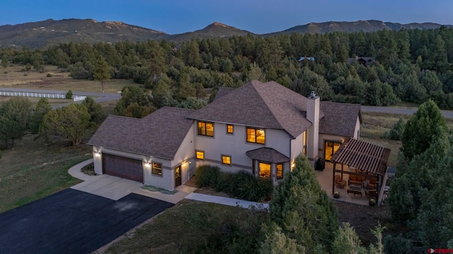 view of front of home with an attached garage, a mountain view, driveway, a chimney, and a wooded view