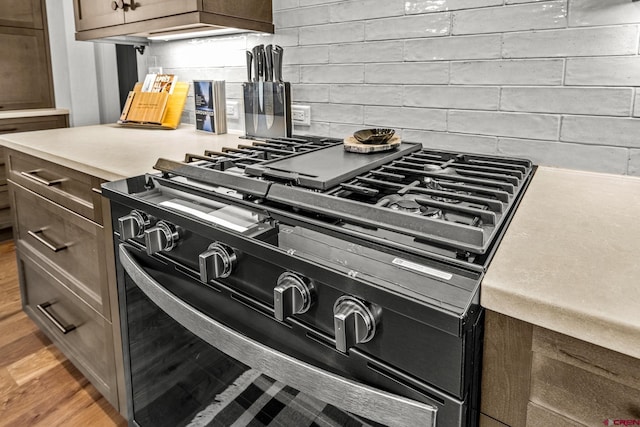 room details featuring light countertops, wood finished floors, black gas stove, and decorative backsplash