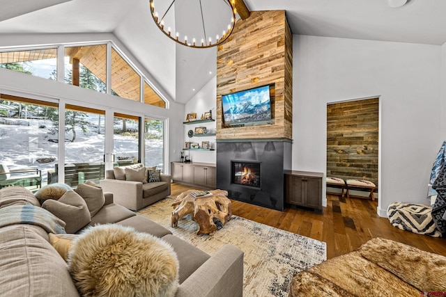 living area with high vaulted ceiling, a large fireplace, wood finished floors, baseboards, and an inviting chandelier