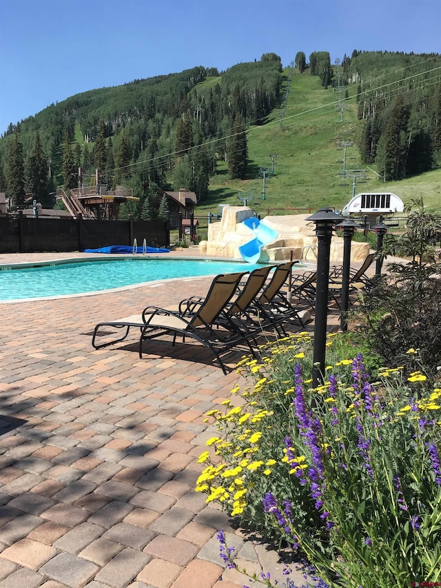 community pool featuring a forest view, fence, and a patio