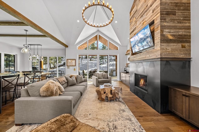 living room with high vaulted ceiling, recessed lighting, a large fireplace, a notable chandelier, and wood finished floors