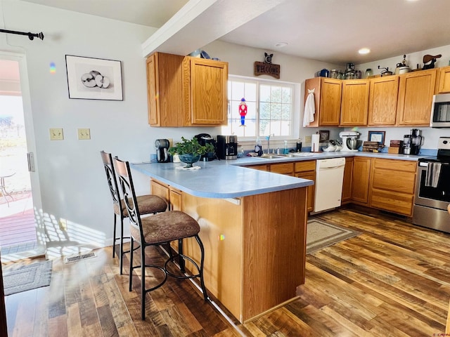 kitchen with a breakfast bar, light countertops, appliances with stainless steel finishes, a sink, and a peninsula