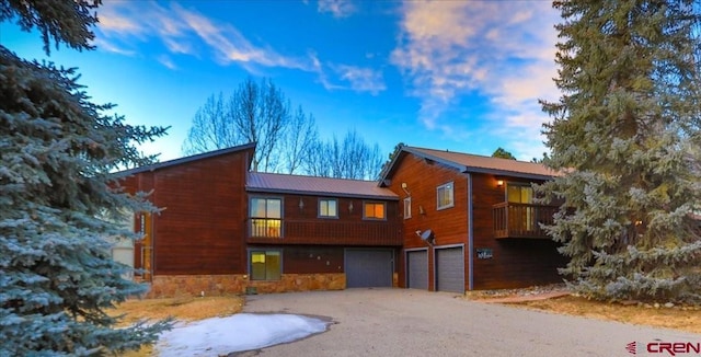 view of front of home with a garage, driveway, metal roof, and stone siding