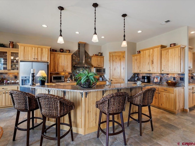 kitchen with a breakfast bar area, visible vents, appliances with stainless steel finishes, wall chimney exhaust hood, and light brown cabinetry