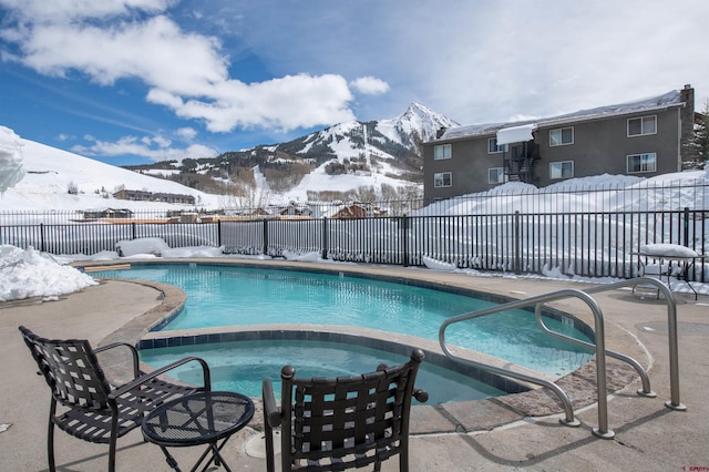 snow covered pool featuring a fenced in pool, an in ground hot tub, a mountain view, and fence