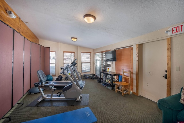 exercise area featuring lofted ceiling, dark colored carpet, and a textured ceiling