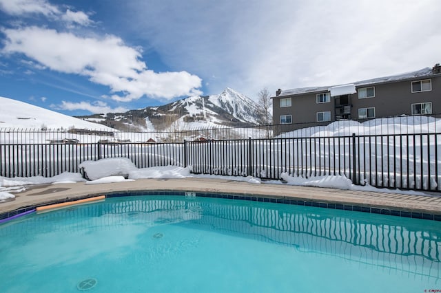 snow covered pool with fence, a mountain view, and a fenced in pool