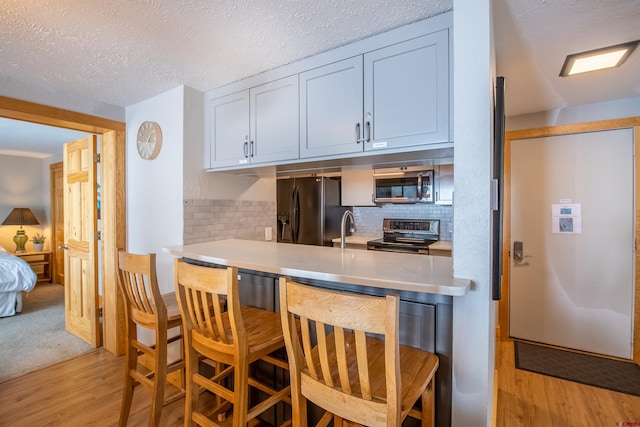 kitchen with light wood-style flooring, white cabinets, light countertops, appliances with stainless steel finishes, and a kitchen bar