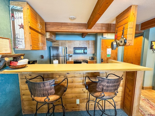 kitchen with black microwave, a peninsula, freestanding refrigerator, beamed ceiling, and a kitchen bar