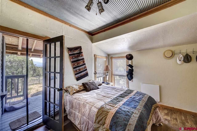 bedroom with a textured wall, wood finished floors, baseboards, access to outside, and ornamental molding