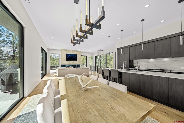 dining space featuring baseboards, a stone fireplace, light wood finished floors, and recessed lighting