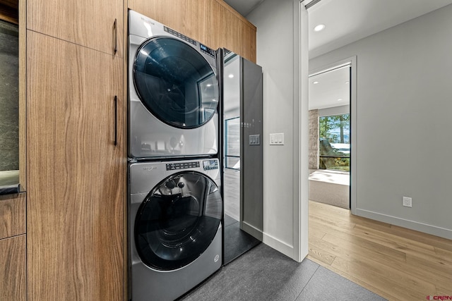 washroom with recessed lighting, laundry area, wood finished floors, baseboards, and stacked washing maching and dryer