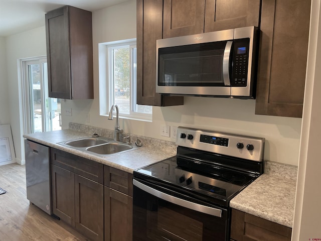 kitchen featuring light wood finished floors, appliances with stainless steel finishes, light countertops, dark brown cabinets, and a sink