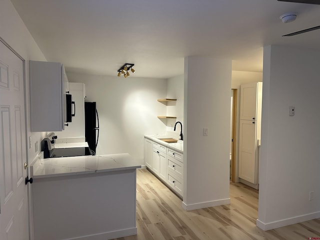 kitchen featuring a sink, white cabinets, light countertops, black appliances, and open shelves