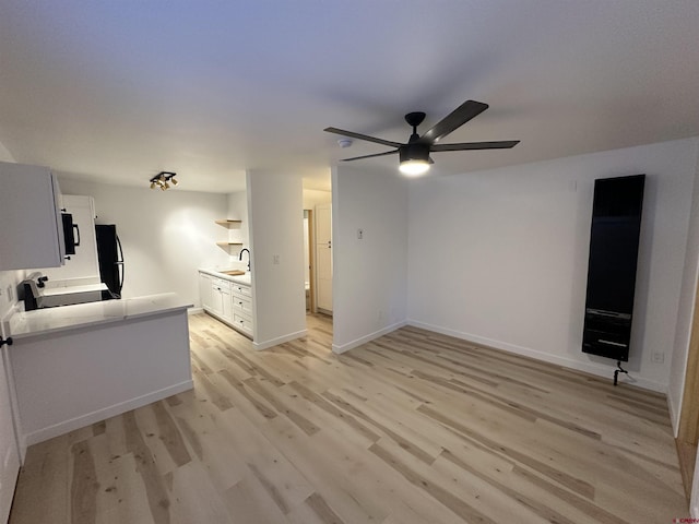 unfurnished living room with light wood-style floors, ceiling fan, baseboards, and a sink