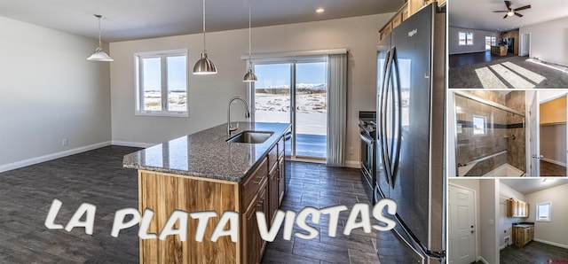 kitchen featuring a kitchen island with sink, a sink, appliances with stainless steel finishes, dark stone counters, and decorative light fixtures