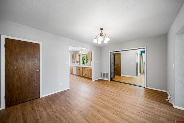 unfurnished room featuring light wood-style floors, baseboards, visible vents, and a notable chandelier