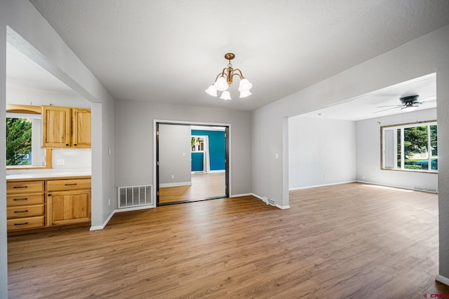 interior space featuring ceiling fan with notable chandelier, light wood-type flooring, visible vents, and baseboards