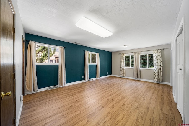 unfurnished bedroom featuring visible vents, light wood-style flooring, a textured ceiling, and multiple windows