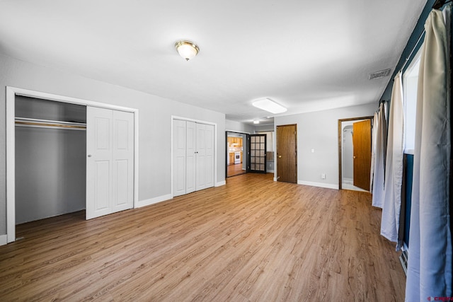 unfurnished bedroom featuring baseboards, light wood-style flooring, visible vents, and multiple closets