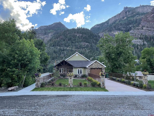 view of front facade featuring stone siding, a fenced front yard, a mountain view, and concrete driveway