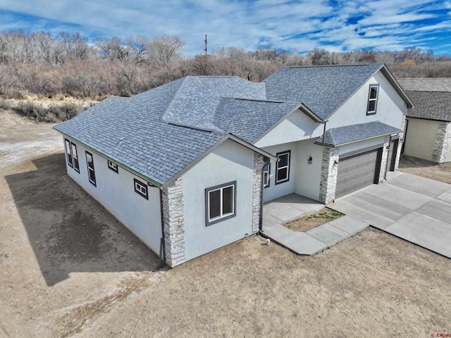 ranch-style house featuring stone siding, a shingled roof, concrete driveway, and stucco siding