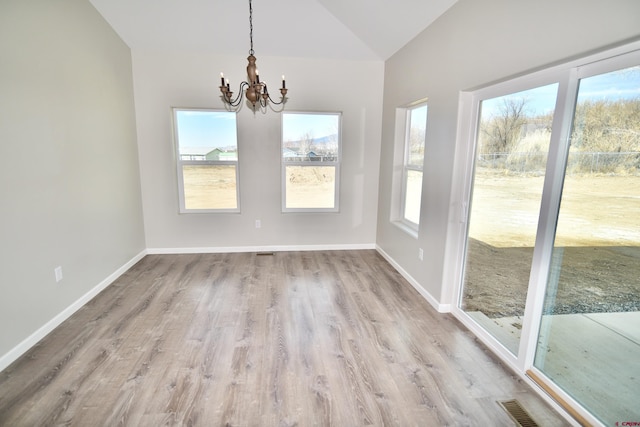 unfurnished dining area featuring light wood-type flooring, a notable chandelier, vaulted ceiling, and baseboards