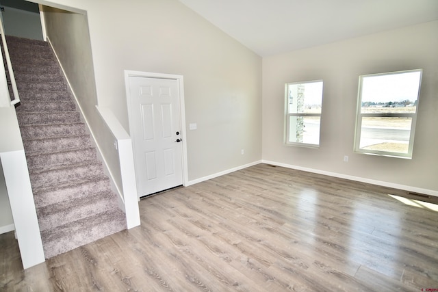 entryway with light wood-style floors, baseboards, stairway, and high vaulted ceiling