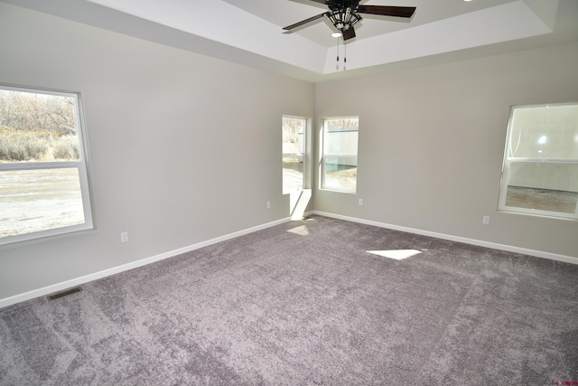 carpeted spare room with a ceiling fan, a raised ceiling, visible vents, and baseboards