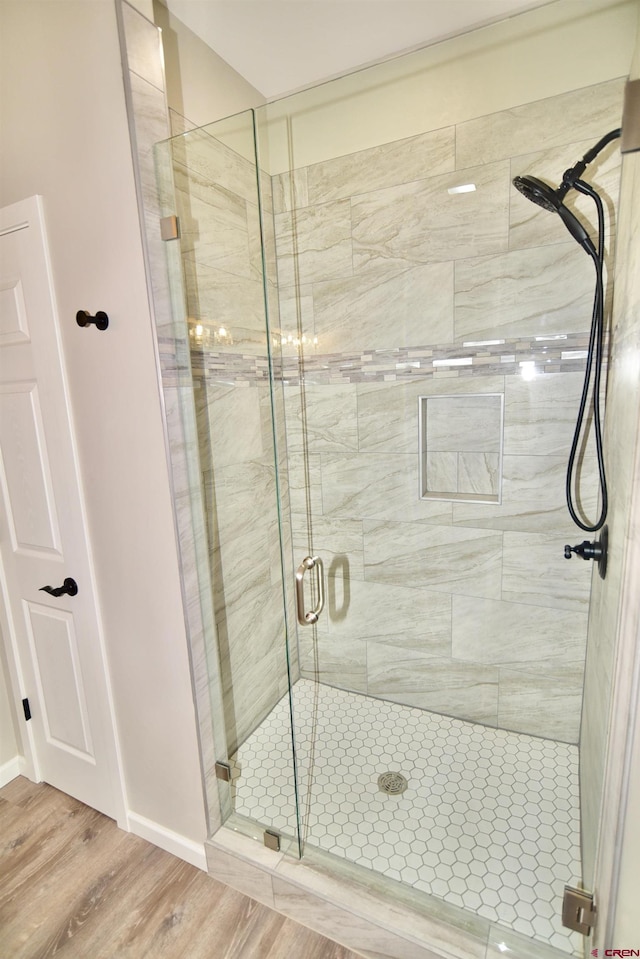 full bath featuring a shower stall, baseboards, and wood finished floors