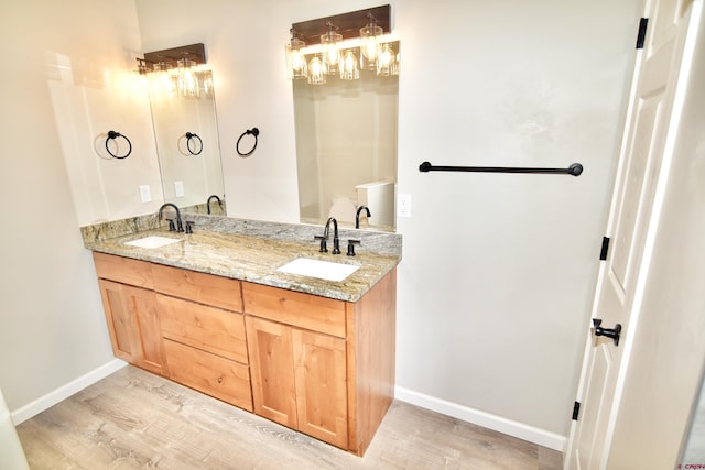 bathroom featuring double vanity, wood finished floors, a sink, and baseboards