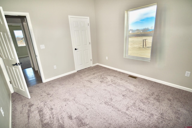 unfurnished bedroom featuring carpet flooring, visible vents, baseboards, and multiple windows