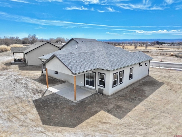 view of front of house with a rural view, roof with shingles, a patio, and stucco siding