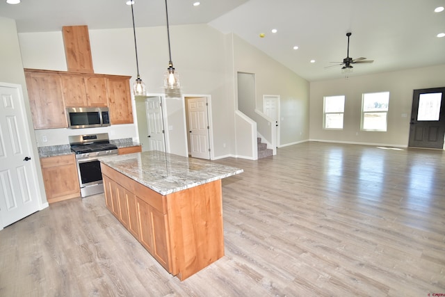 kitchen with light stone counters, stainless steel appliances, a kitchen island, open floor plan, and hanging light fixtures