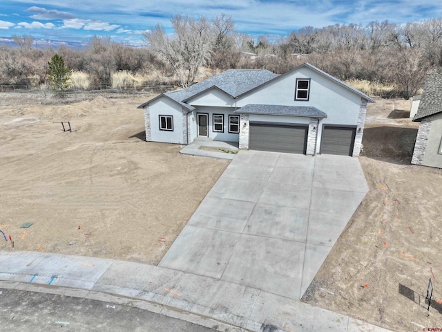 view of front facade featuring driveway, stone siding, roof with shingles, an attached garage, and stucco siding