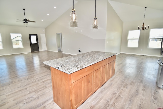 kitchen with light stone counters, open floor plan, hanging light fixtures, light wood-type flooring, and high vaulted ceiling